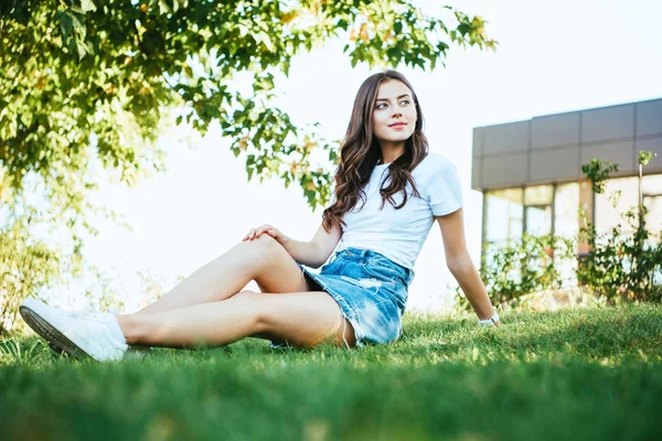 Schönes Mädchen sitzt auf grünem Gras im Park und schaut weg — Stockfoto