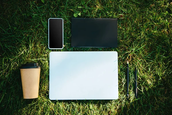 Erhöhter Blick auf digitale Geräte und Einweg-Kaffeetasse auf grünem Gras im Park — Stockfoto