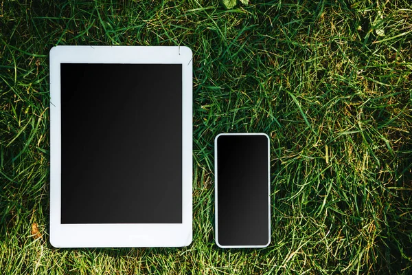 Elevated view of tablet and smartphone with blank screens on green grass in park — Stock Photo
