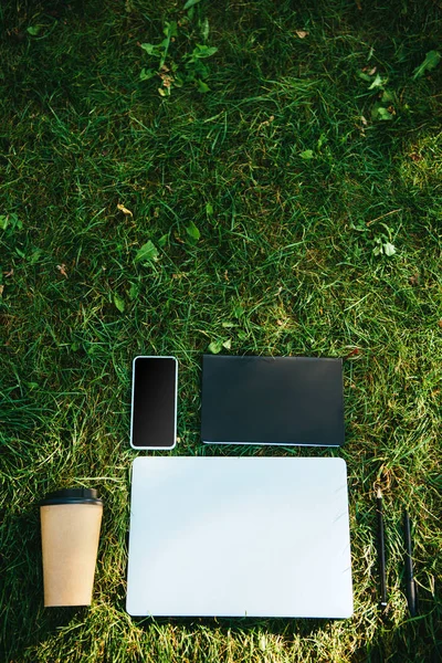 Erhöhte Ansicht von Gadgets und Kaffee in Pappbecher auf grünem Gras im Park — Stockfoto