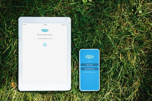 Elevated view of tablet and smartphone with loaded skype pages on green grass in park — Stock Photo