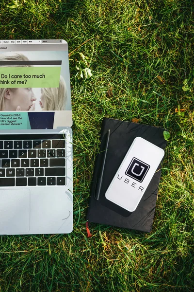 Top view of laptop with website and smartphone with uber appliance on green grass in park — Stock Photo