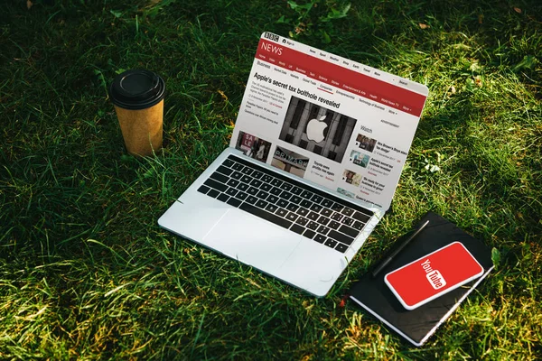 Laptop mit bbc News und Smartphone mit Youtube-Seite auf grünem Gras im Park — Stockfoto