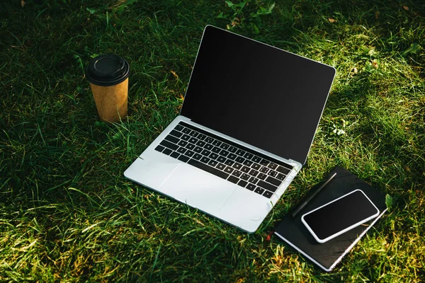 Geräte mit leeren Bildschirmen und Kaffee in Pappbecher auf grünem Gras im Park — Stockfoto