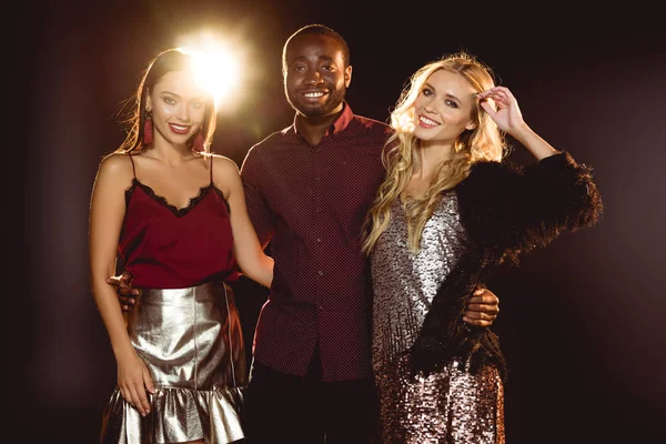 Souriant homme afro-américain étreignant deux jolies femmes sur noir avec rétro-éclairé — Photo de stock