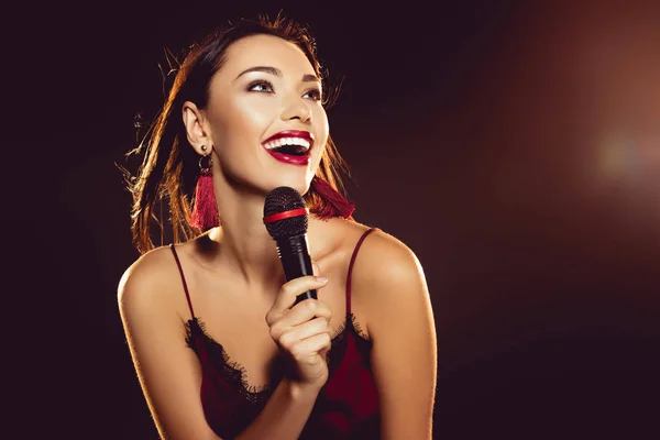 Retrato de mujer joven y feliz con micrófono en la mano cantando karaoke - foto de stock