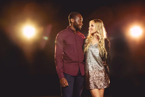 Lächelndes multikulturelles Paar, das sich auf schwarz mit Gegenlicht anschaut — Stockfoto