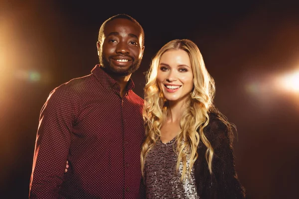 Multicultural couple looking at camera on black with backlit — Stock Photo