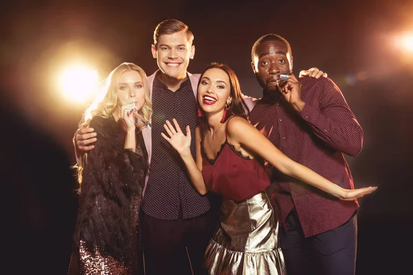 Luxury multiethnic friends celebrating new year with party horns on black with backlit — Stock Photo