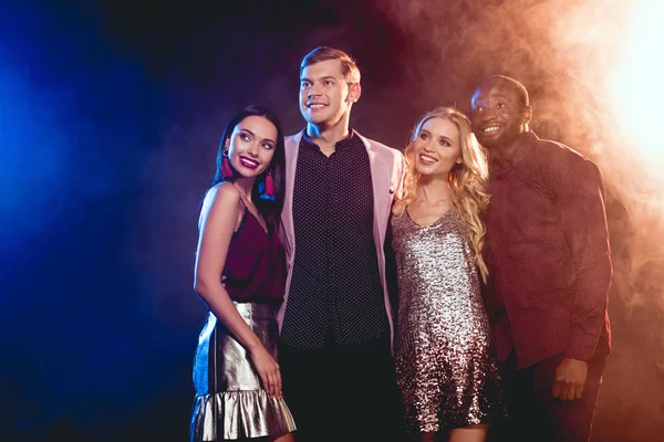 Bela sorrindo amigos multiétnicos abraçando na festa com fumaça — Fotografia de Stock