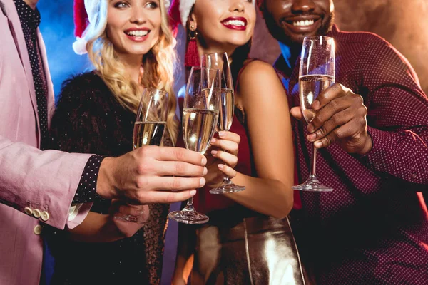 Multiethnische Freunde in Weihnachtsmützen klirren mit Sektgläsern auf der Neujahrsparty — Stockfoto