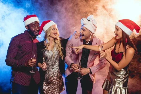Amigos multiculturales emocionados en sombreros de santa con copas de champán en la fiesta de año nuevo - foto de stock