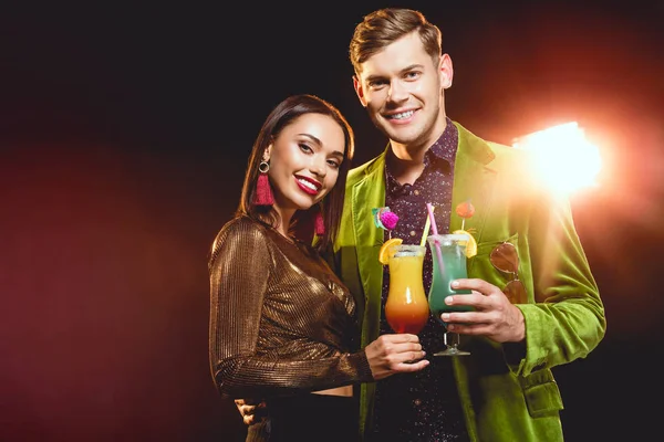 Beautiful glamorous couple clinking with cocktail glasses on party with back light — Stock Photo