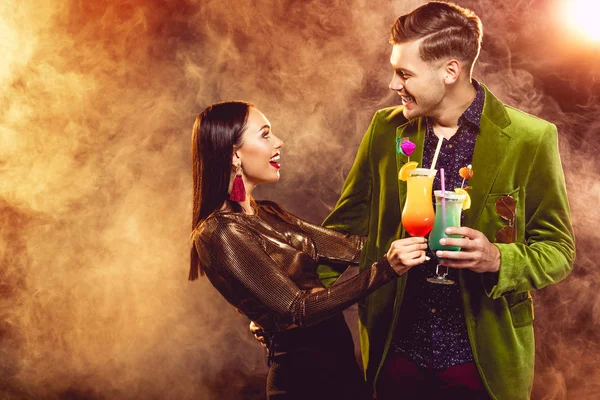 Excitada pareja glamorosa tintineo con copas de cóctel en fiesta con humo - foto de stock