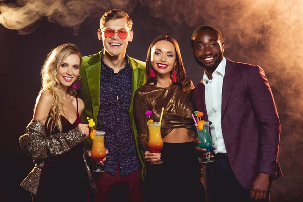 Sonrientes amigos multiculturales sosteniendo cócteles de alcohol en la fiesta - foto de stock