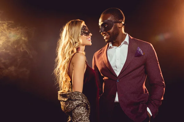 Beautiful multicultural couple in carnival masks for new year party with backlit — Stock Photo