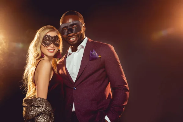 Feliz casal multicultural em máscaras de carnaval para a festa de ano novo — Fotografia de Stock