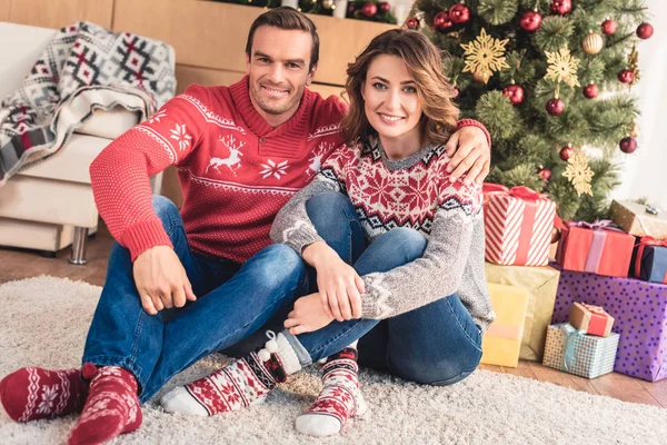 Sorrindo marido e mulher olhando para a câmera em casa com árvore de natal no fundo — Fotografia de Stock