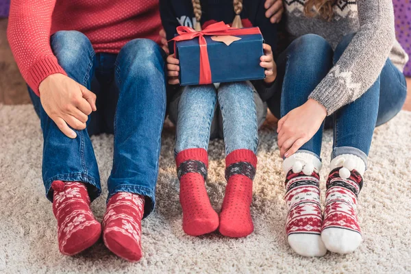 Cropped image of parents and daughter in winter clothes sitting with present at home — Stock Photo