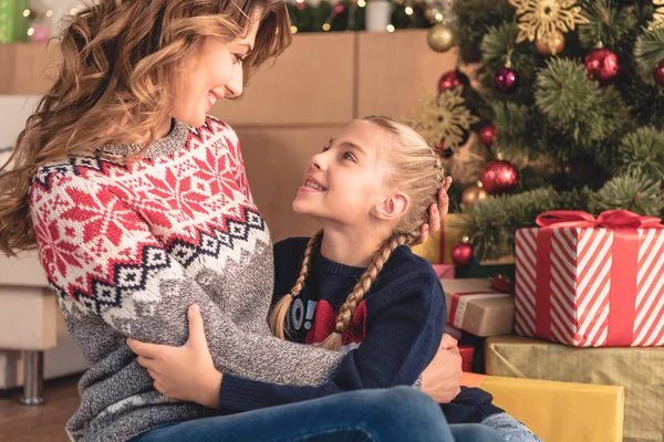 Mutter und Tochter umarmen sich am Weihnachtsbaum und schauen sich zu Hause an — Stockfoto