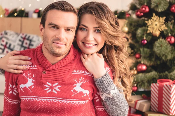 Sorrindo esposa abraçando marido e olhando para a câmera em casa, árvore de natal no fundo — Fotografia de Stock