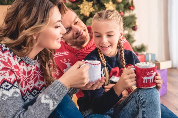 Padres felices y la hija sentada con copas de Navidad de capuchino en casa - foto de stock