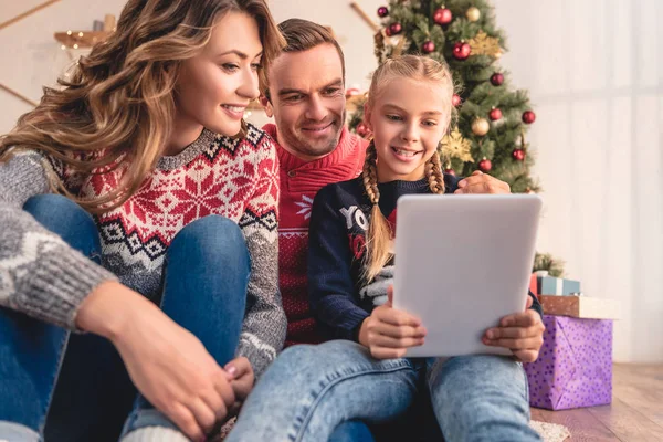 Happy parents and daughter using tablet together near christmas tree at home — Stock Photo