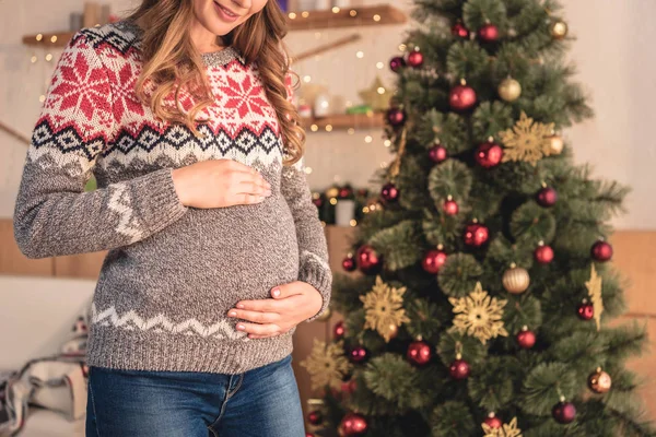 Imagem cortada de mulher grávida em santa chapéu tocando barriga em casa — Fotografia de Stock