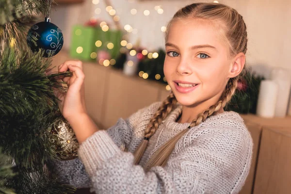 Adorável criança pré-adolescente decoração árvore de natal em casa e olhando para a câmera — Fotografia de Stock