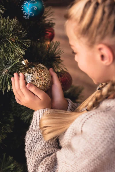 Selektiver Fokus eines entzückenden Frühchens, das zu Hause eine goldene Christbaumkugel in den Händen hält — Stockfoto