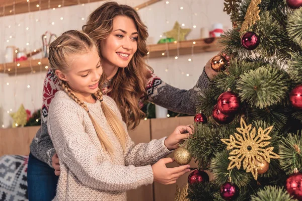 Glückliche Mutter und Tochter in Pullovern schmücken Weihnachtsbaum zu Hause mit Christbaumkugeln — Stockfoto