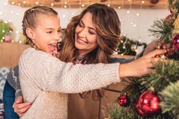 Happy mother and excited daughter decorating christmas tree with baubles at home — Stock Photo