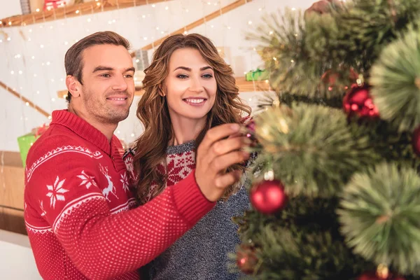 Sorrindo casal em suéteres decorando árvore de natal em casa — Fotografia de Stock