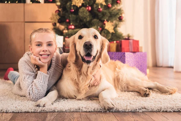 Glückliches Kind und Golden Retriever Hund liegen neben Weihnachtsbaum mit Geschenken zu Hause — Stockfoto