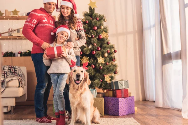 Glückliche Familie in Weihnachtsmützen mit Golden Retriever Hund in Hirschhörnern posiert zu Hause in der Nähe des Weihnachtsbaums mit Geschenken — Stockfoto