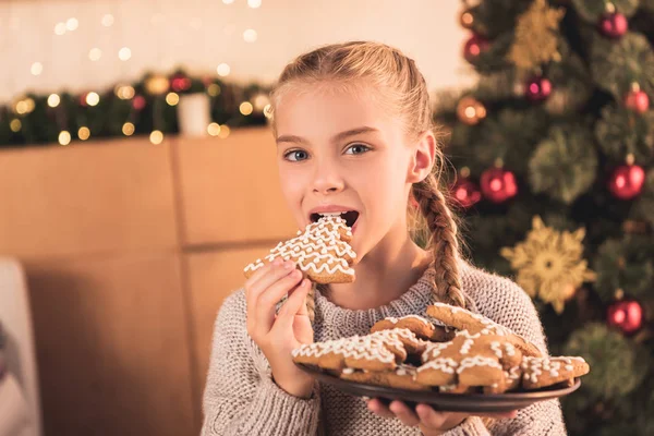 Adorable preteen kid eating cookie and holding plate with traditional christmas gingerbread cookies — Stock Photo