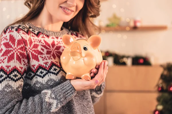 Cropped view of woman in christmas sweater holding big piggy bank — Stock Photo