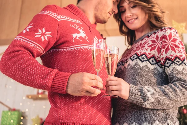 Casal feliz em camisolas de Natal clinking com copos de champanhe — Fotografia de Stock