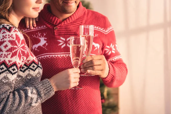 Cropped view of couple in christmas sweaters holding glasses with champagne — Stock Photo