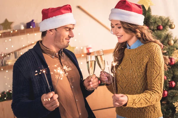 Hermosa pareja en sombreros de santa celebrando la Navidad con champán y bengalas - foto de stock