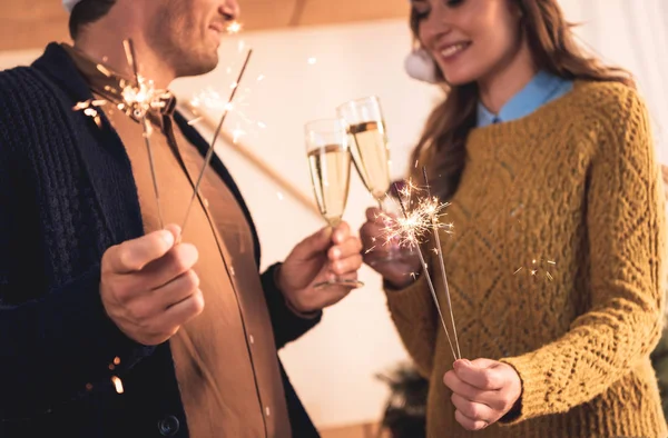 Vista recortada de la pareja que celebra el año nuevo con copas de champán y bengalas - foto de stock