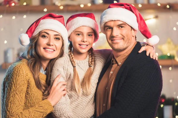 Smiling family in santa hats hugging at christmastime — Stock Photo