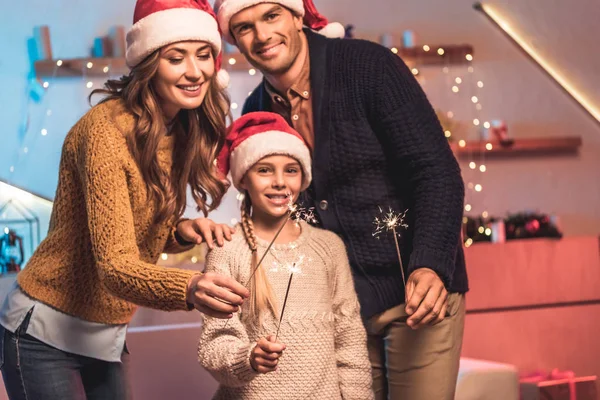 Familia feliz en los sombreros de santa celebrando con chispas de año nuevo - foto de stock