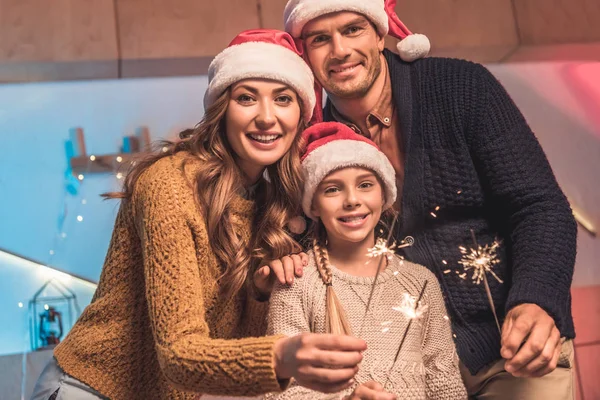 Cheerful family in santa hats celebrating christmas with sparklers — Stock Photo
