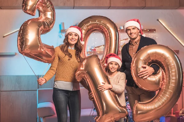 Alegre familia con hija en santa sombreros celebración 2019 año nuevo oro globos - foto de stock