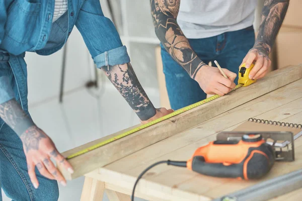 Cropped shot of tattooed couple working with wooden plank and measuring tape — Stock Photo