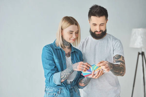 Sorridente giovane coppia tatuata scegliere i colori per la riparazione della casa — Foto stock