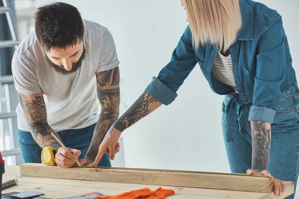 Jeune couple travaillant avec planche en bois et ruban à mesurer — Photo de stock