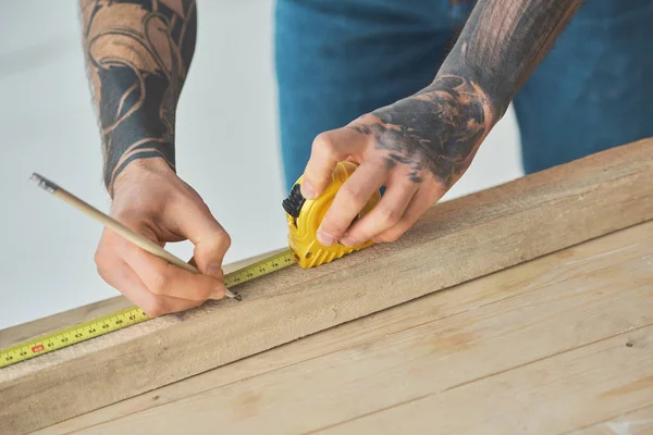 Cropped shot of man holding pencil and measuring tape while working with wooden planks — Stock Photo
