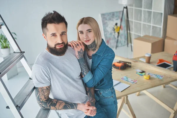 Visão de alto ângulo de belo jovem casal tatuado sorrindo para a câmera enquanto estão juntos em nova casa — Fotografia de Stock